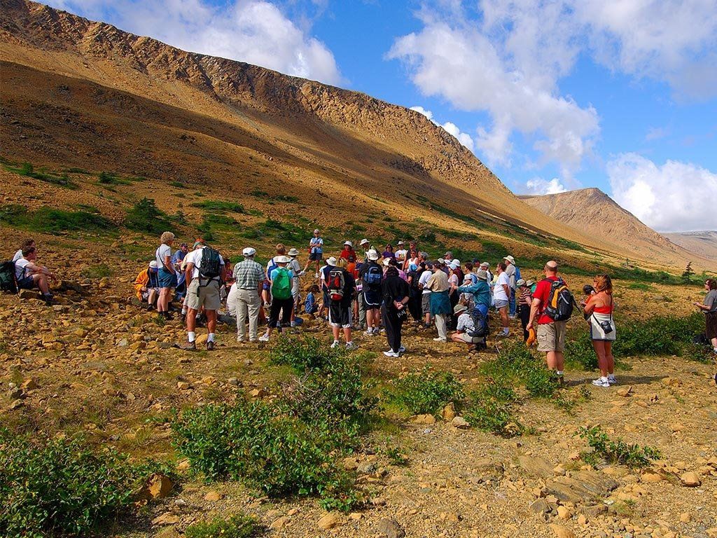 Group of hikers on a rocky, brown mountainside under a blue sky.
