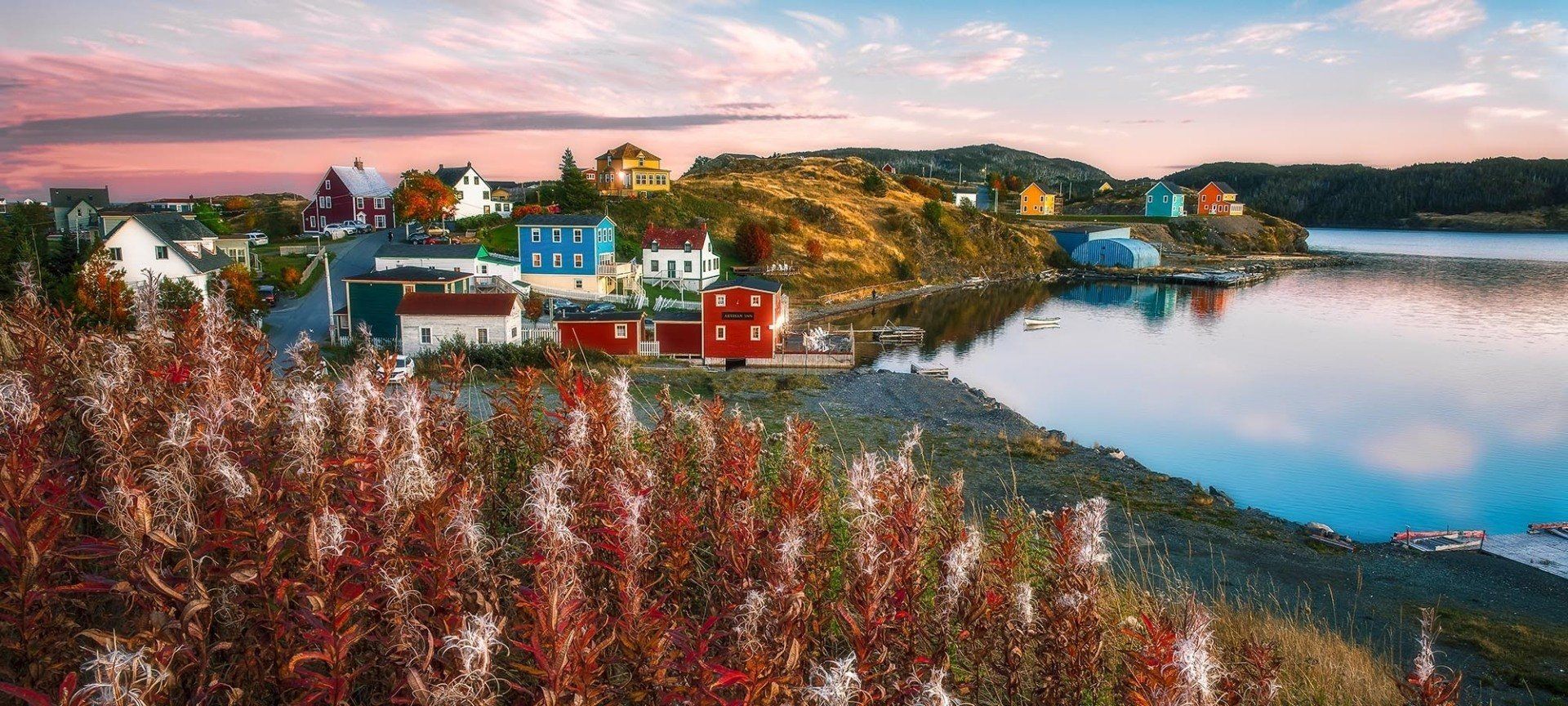 Colorful coastal village at dawn with a reflective bay and fall foliage.