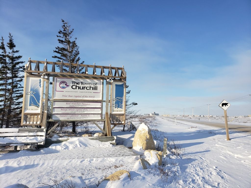 Sign for The Journey Church in snowy Churchill, Manitoba, with a bear warning sign nearby.