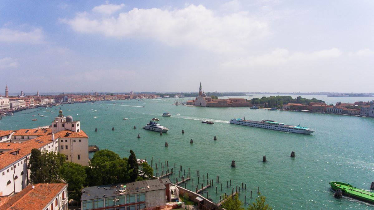 Venice, Italy: Boats on turquoise water, buildings with red-tiled roofs, sunny day, island in the distance.