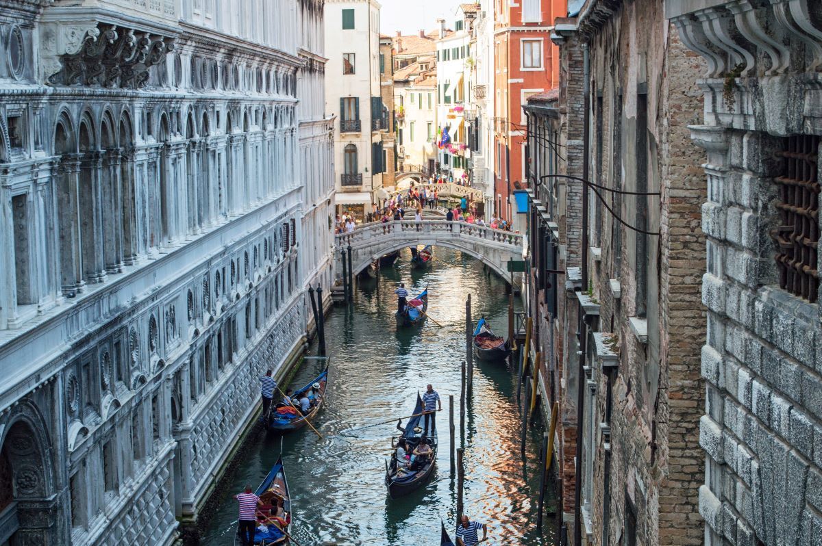Venice canal with gondolas under a stone bridge, flanked by buildings in Italy.