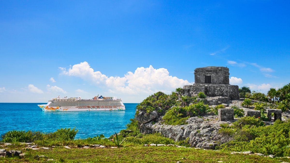Cruise ship near ancient ruins on a cliff overlooking the blue ocean under a sunny sky.
