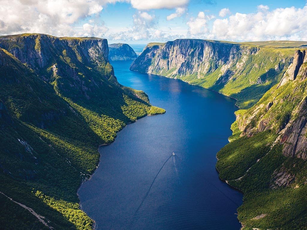Deep blue fjord winding between steep, forested cliffs. A small boat sails on the water.