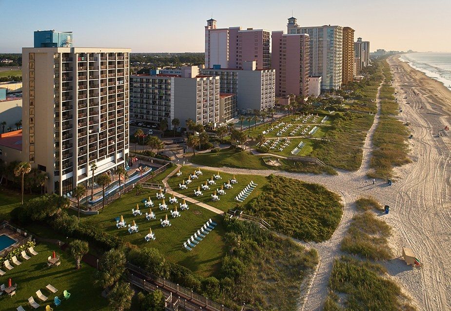 Coastal resort with tall hotels, beach, and manicured green spaces.