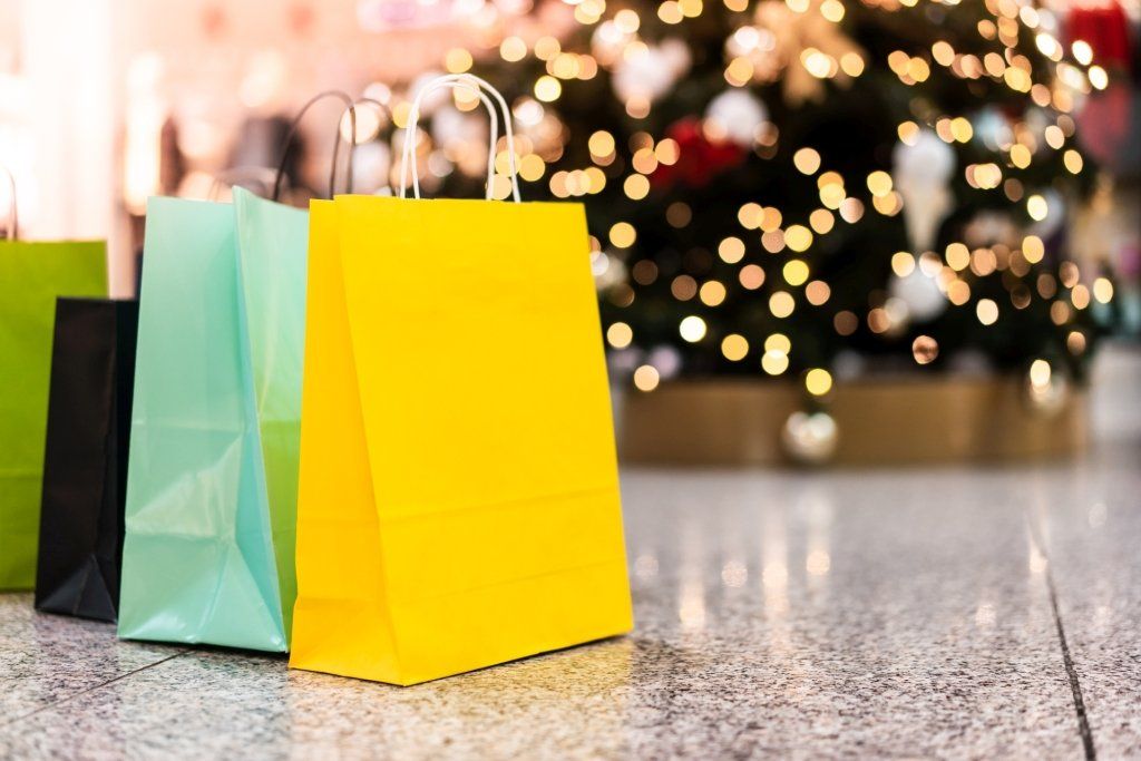 Shopping bags in various colors in front of a Christmas tree with bokeh lights.