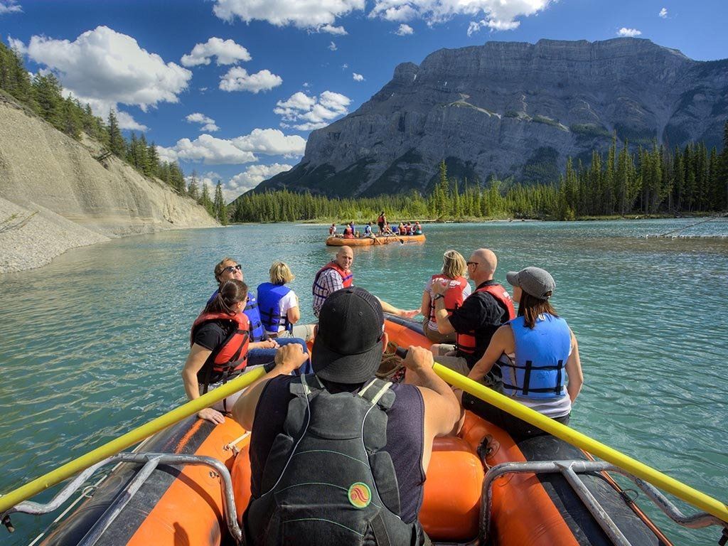 People rafting on a turquoise river near mountains on a sunny day.