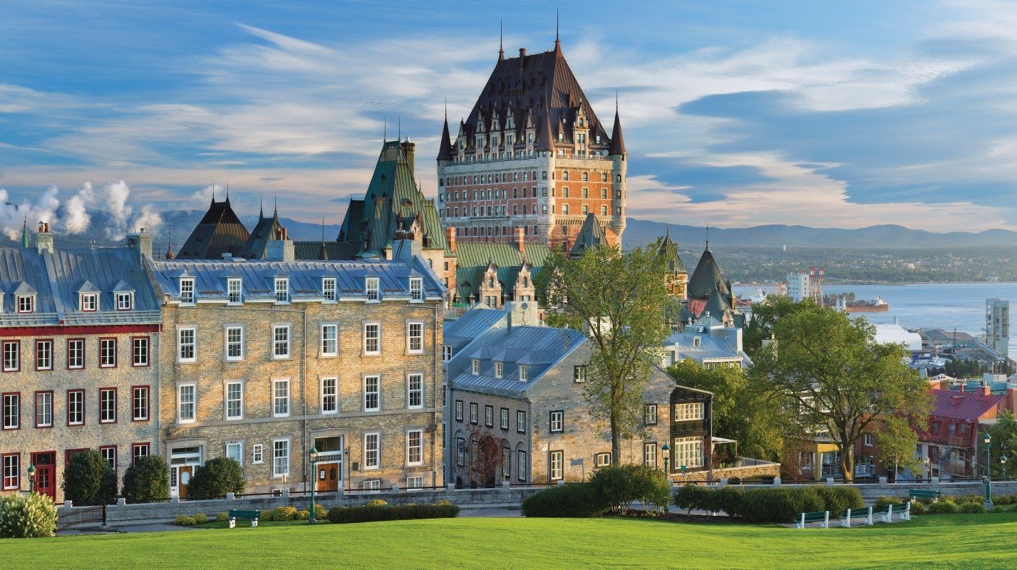 Historic stone buildings and a grand château on a hill overlooking a river at sunset