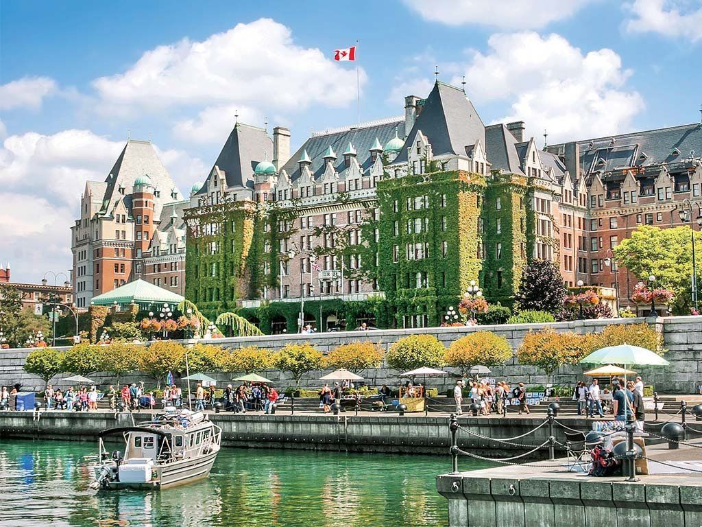 The Fairmont Empress Hotel in Victoria, BC, Canada, with a harbor, boats, and people on a sunny day.