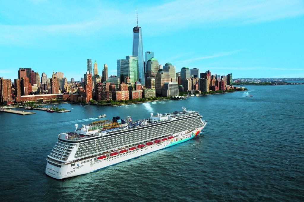 Cruise ship sailing in front of the New York City skyline on a sunny day.
