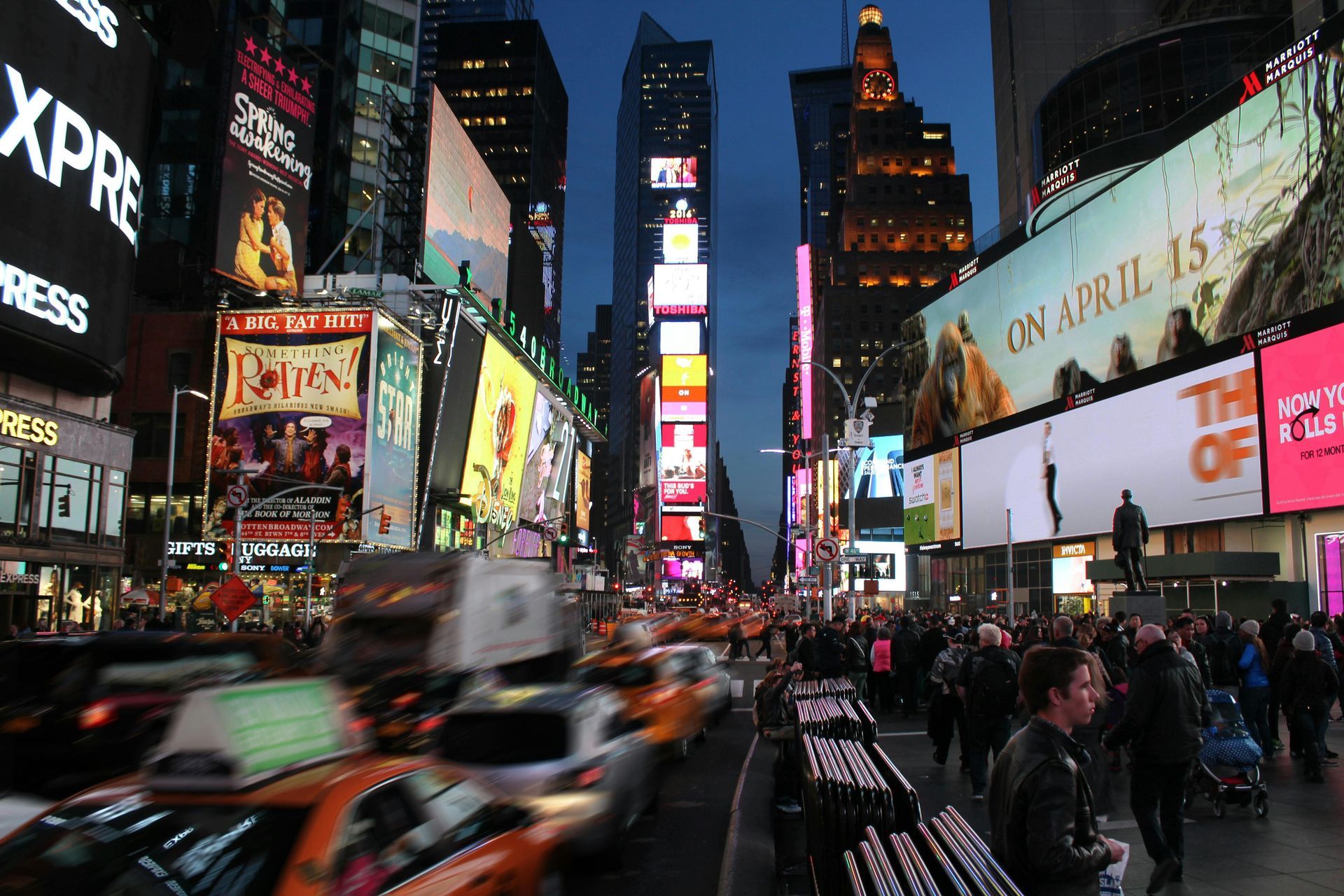 Times Square at night, illuminated by bright billboards, with traffic and crowds of people.