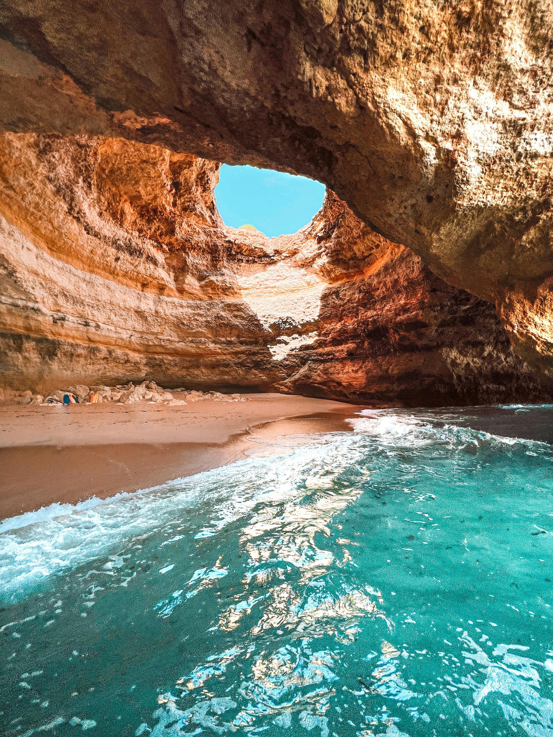Turquoise water under a rocky sea cave with a sandy beach and bright blue sky opening