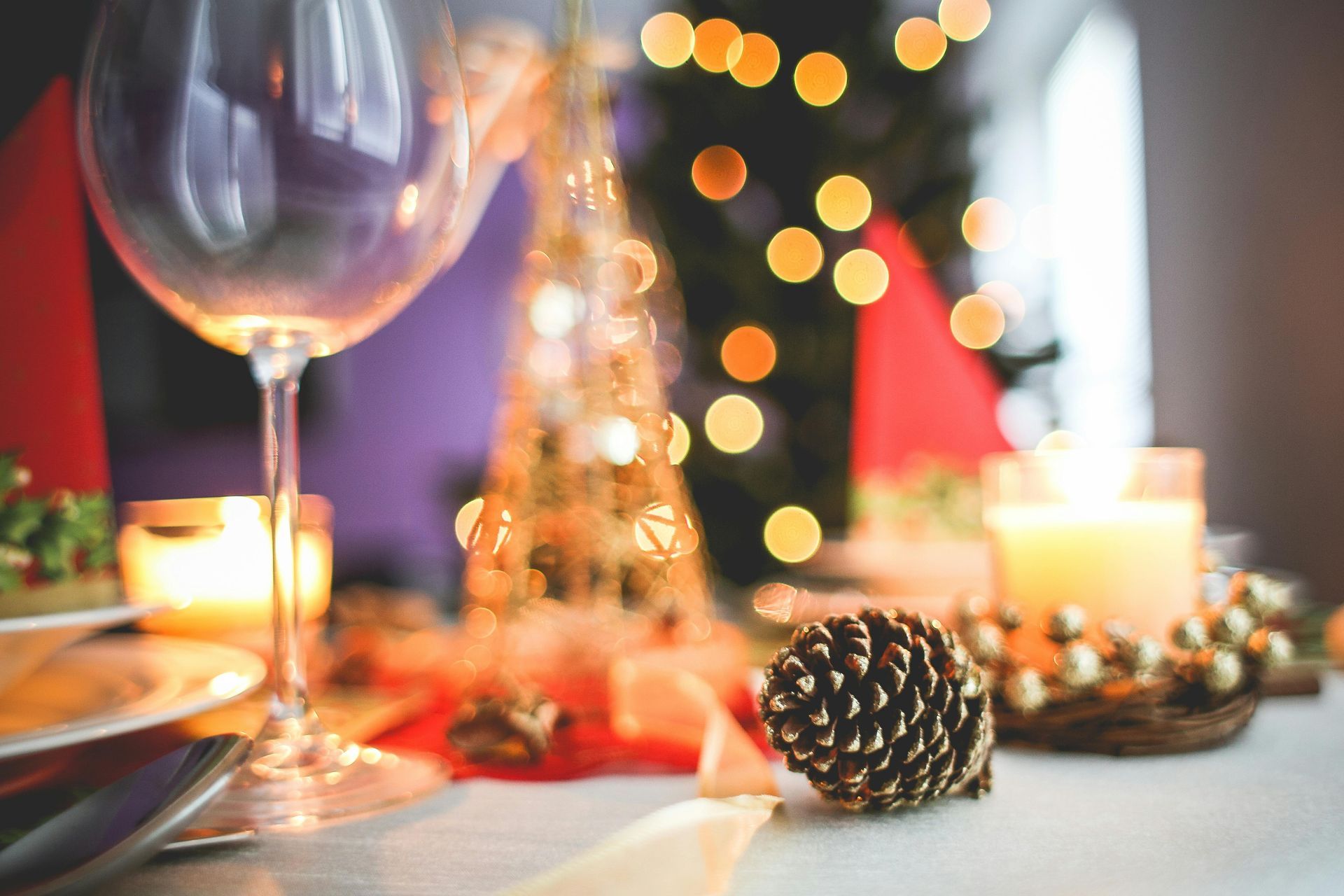 Festive Christmas table setting with a wine glass, candle, and pinecone. Soft bokeh lights in the background.