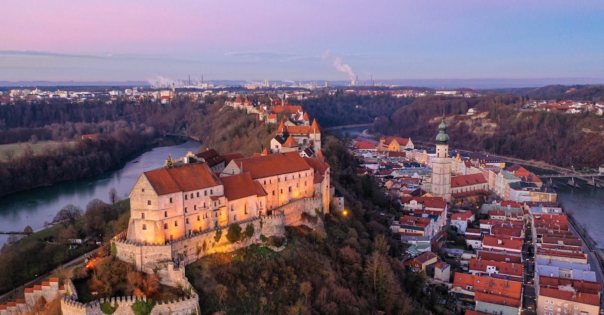 Aerial view of Passau, Germany at dusk, with illuminated Veste Oberhaus fortress overlooking the city and river.