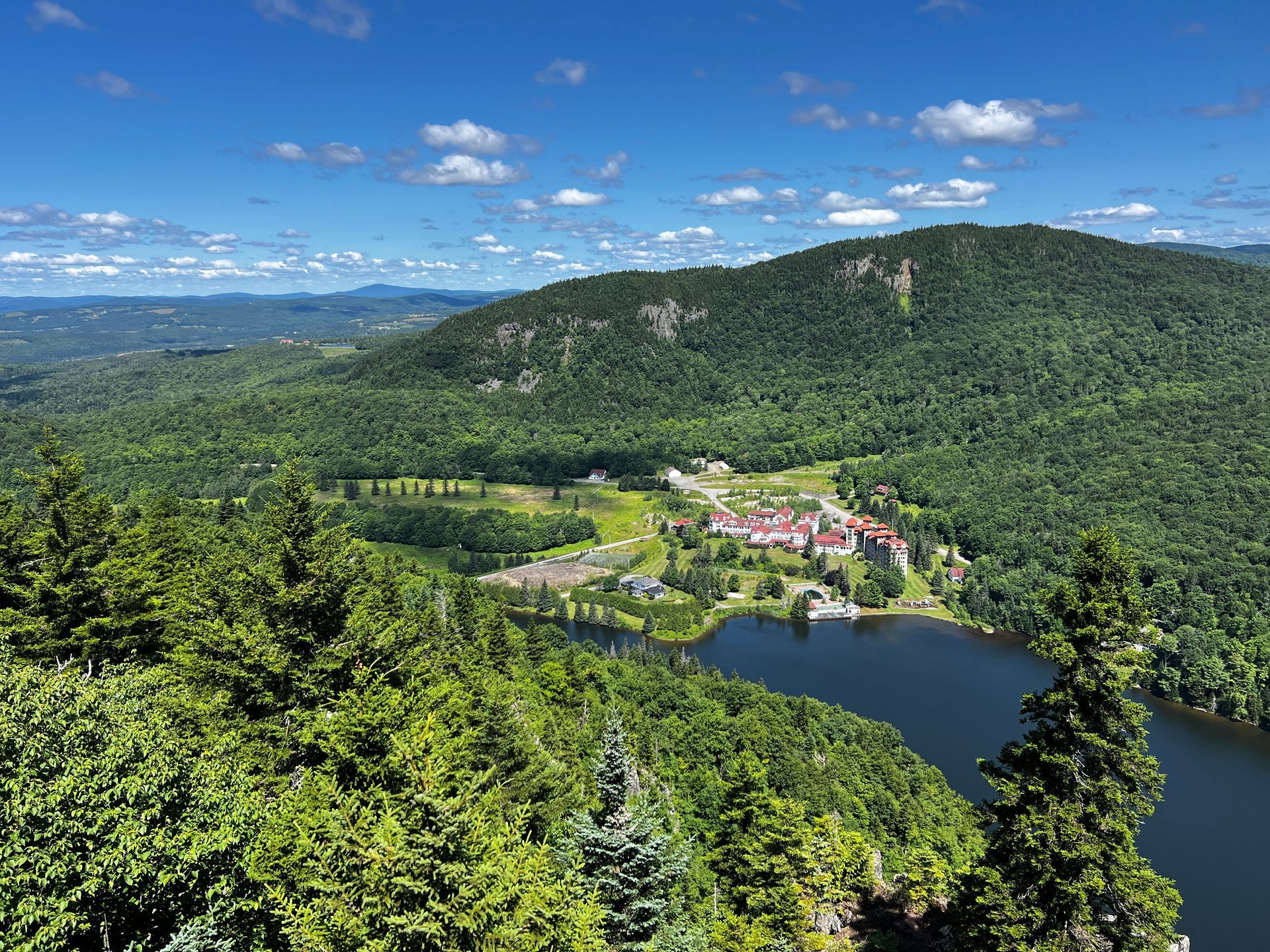 Panoramic view of a lake, forested hills, and a small resort under a blue sky