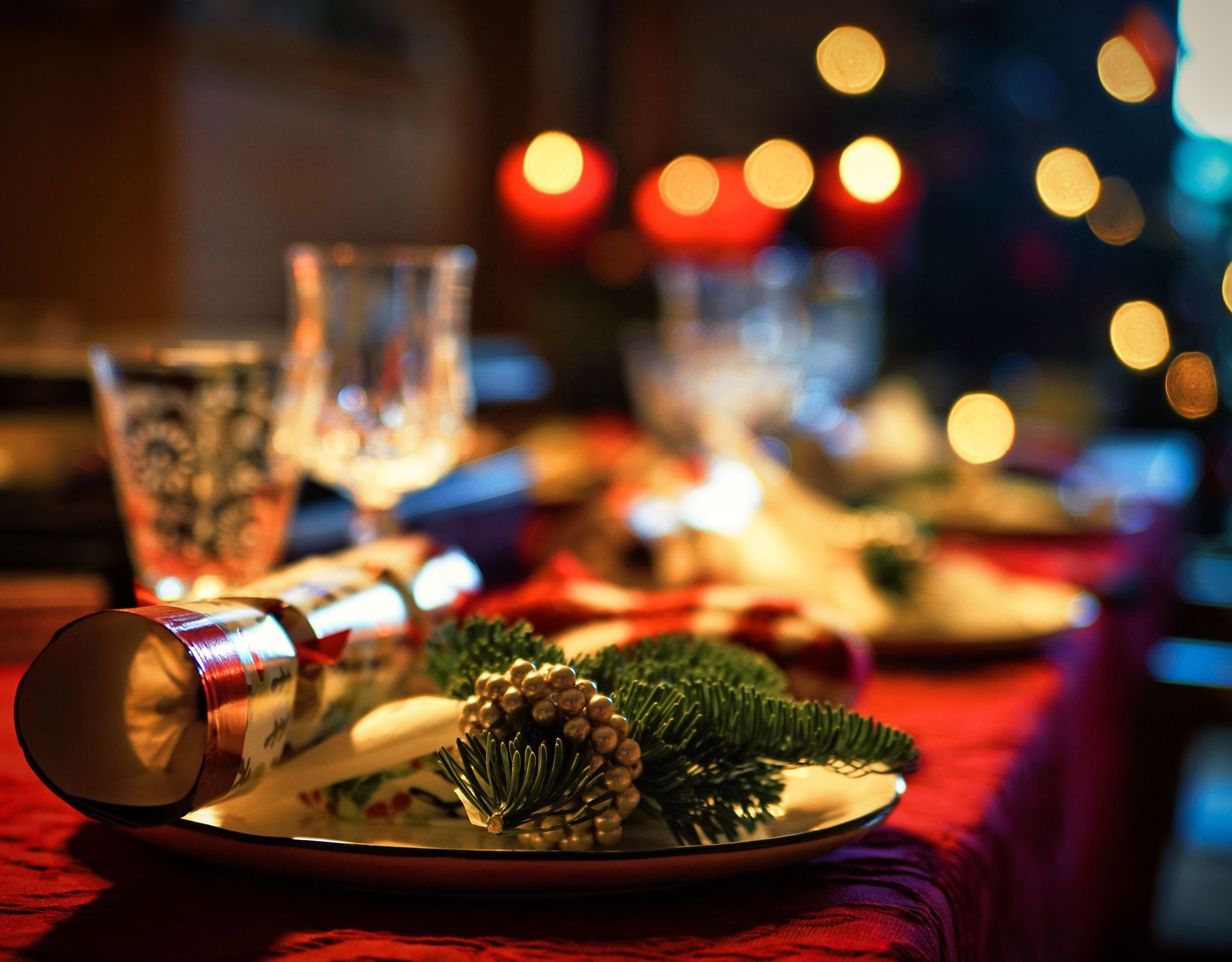 Festive candlelit dining table with red tablecloth, glasses, plates, and holiday decor