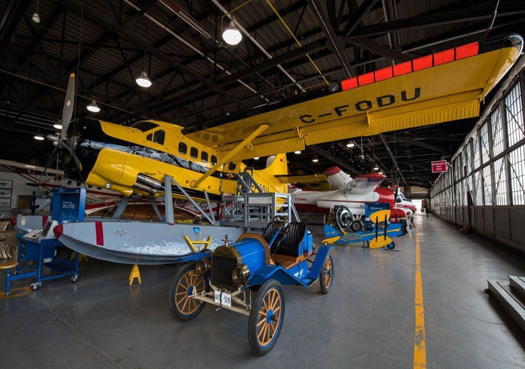 Yellow and blue airplane in hangar with a classic blue car.