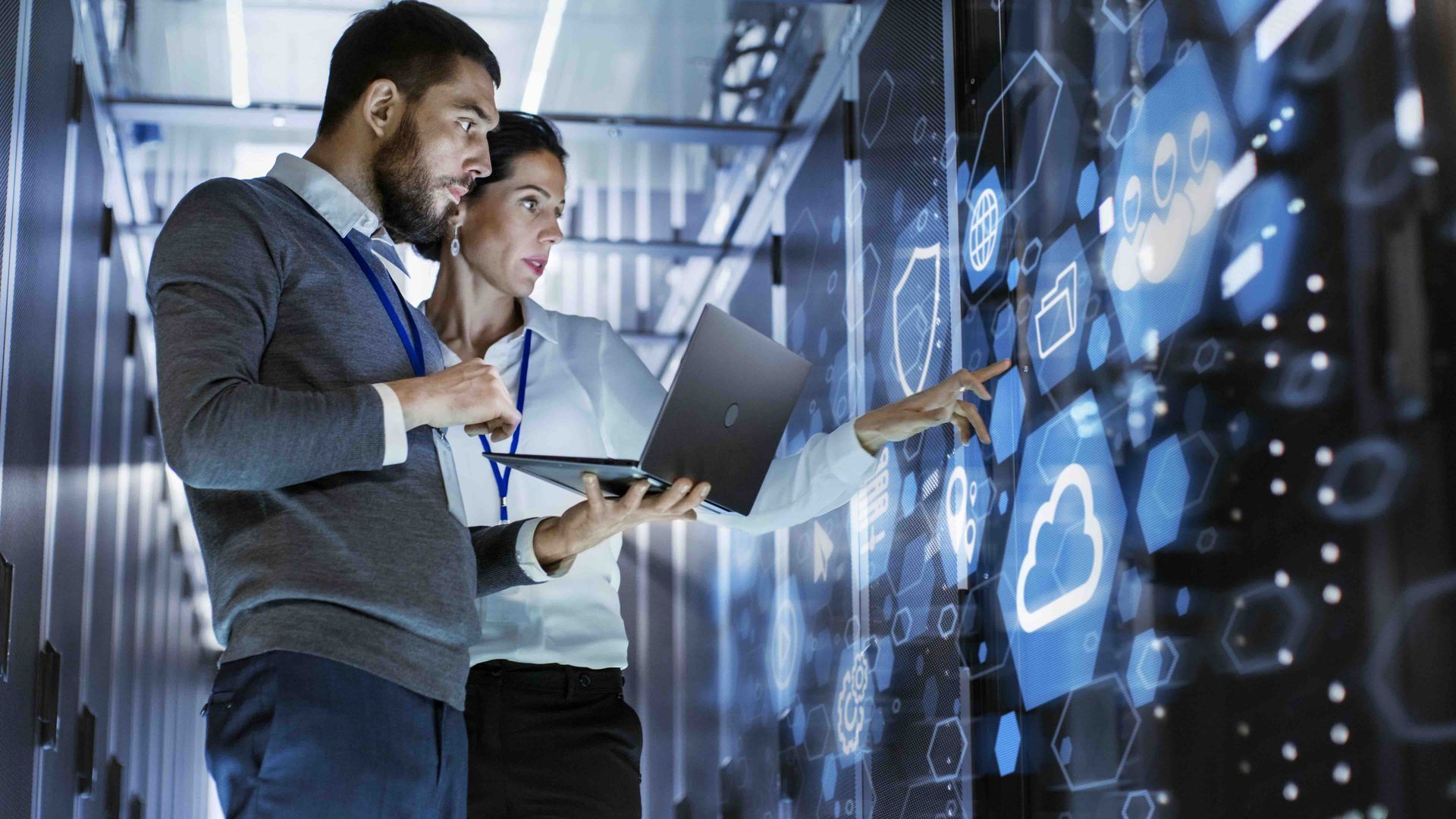 Two professionals reviewing data on a laptop beside a glowing digital dashboard in an office
