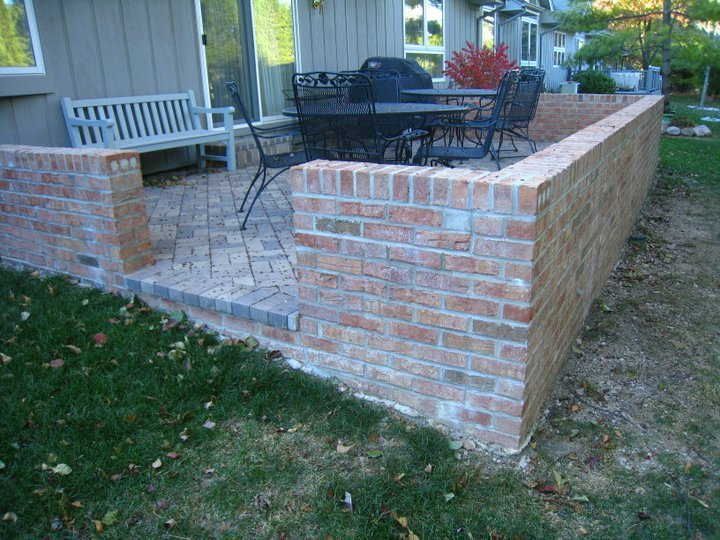 A brick wall surrounds a patio with a table and chairs.