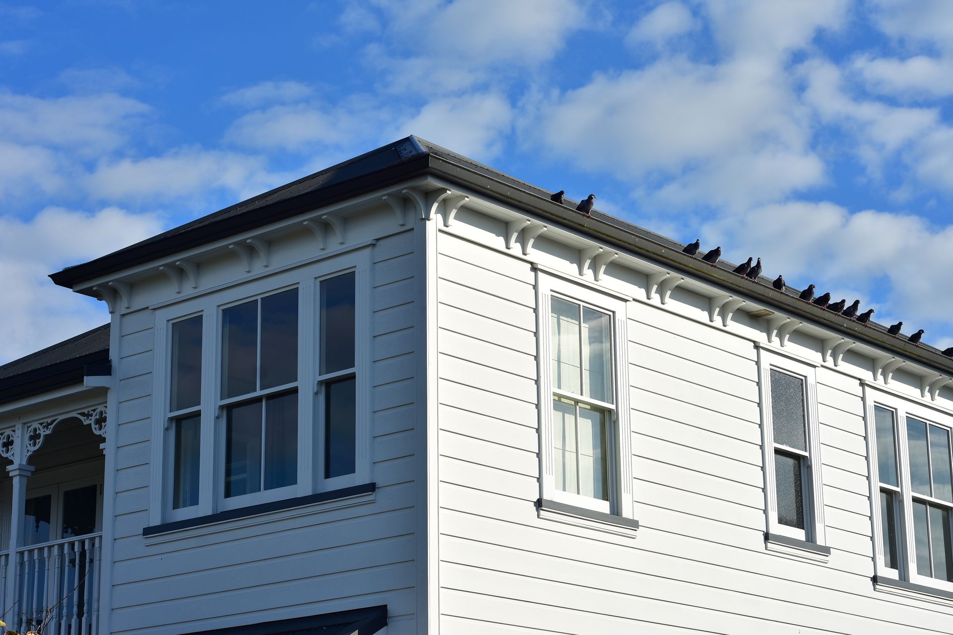 A white house with many windows and birds on the roof