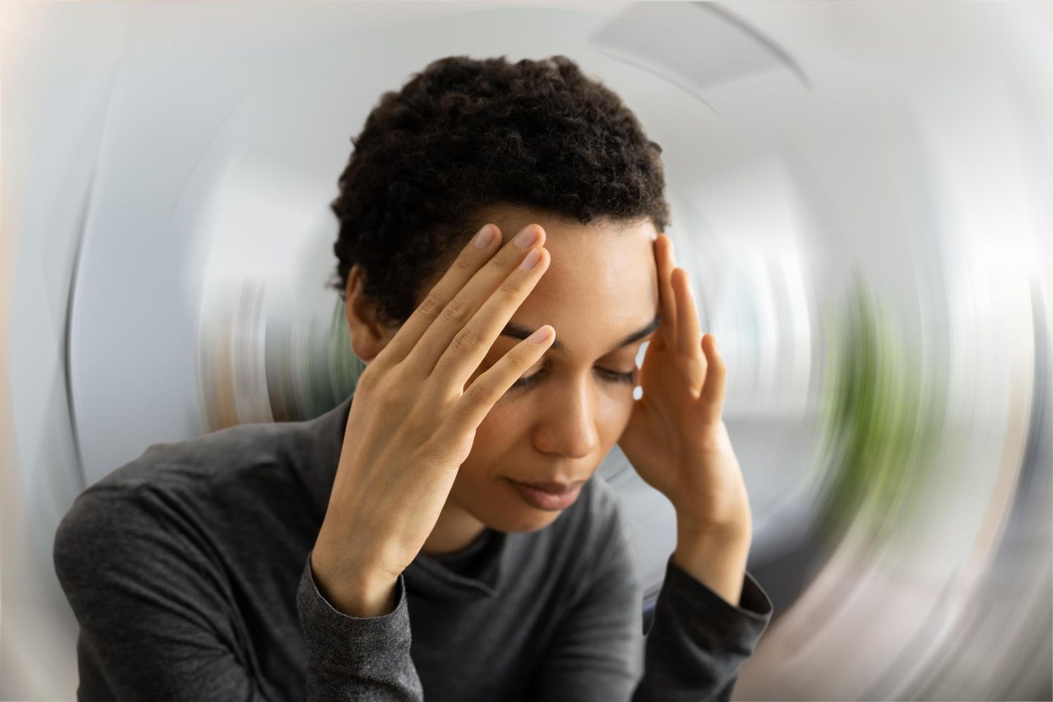 A person holding their head with both hands, eyes closed, against a motion-blurred, swirling background.