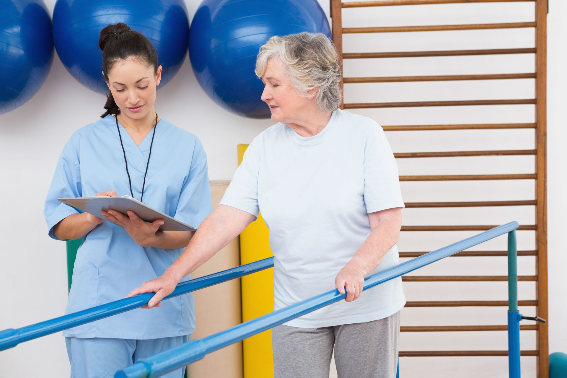 Therapist and patient in a rehab room, standing by parallel bars during gait training.