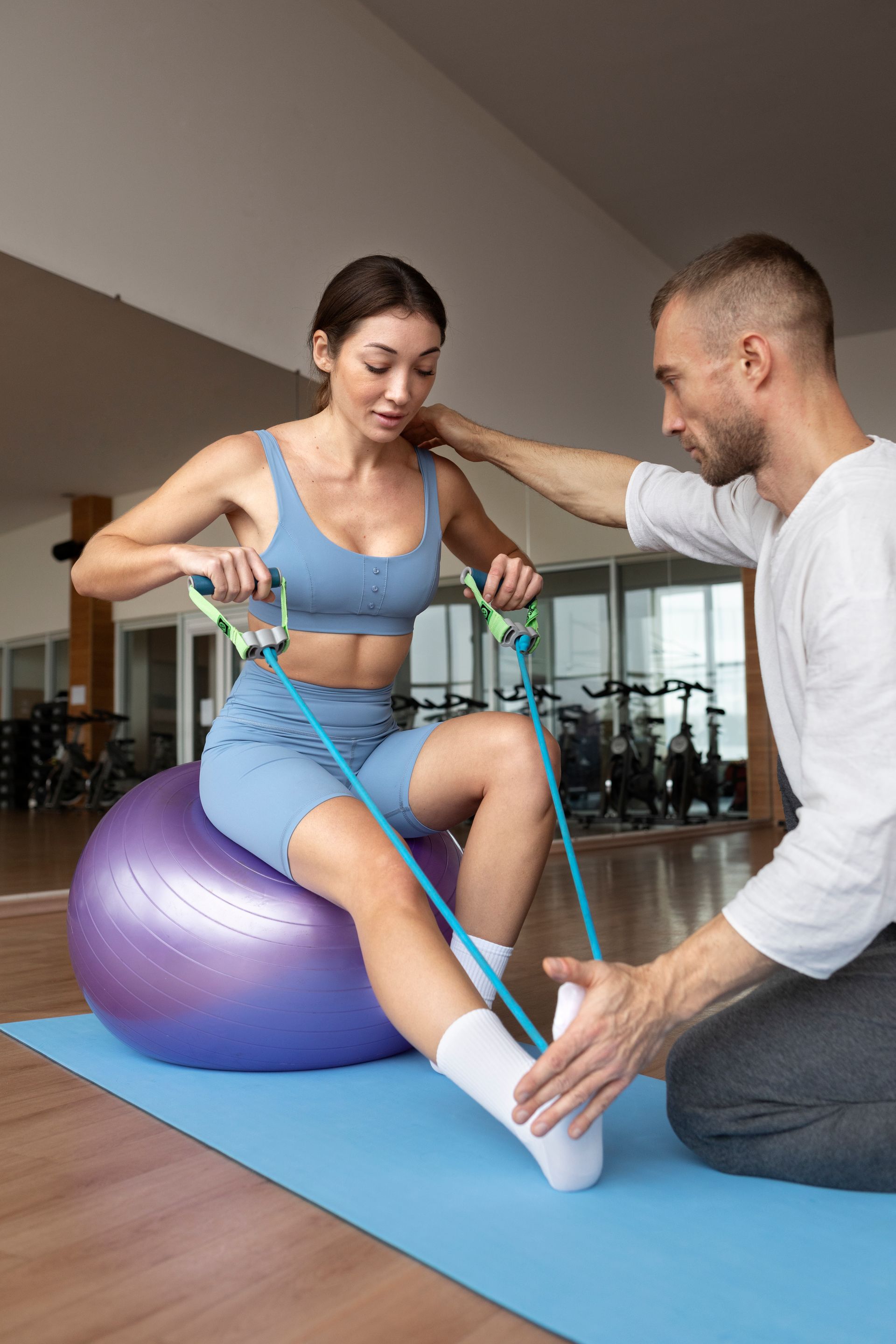 a woman sits on a purple exercise ball while a man stretches her leg