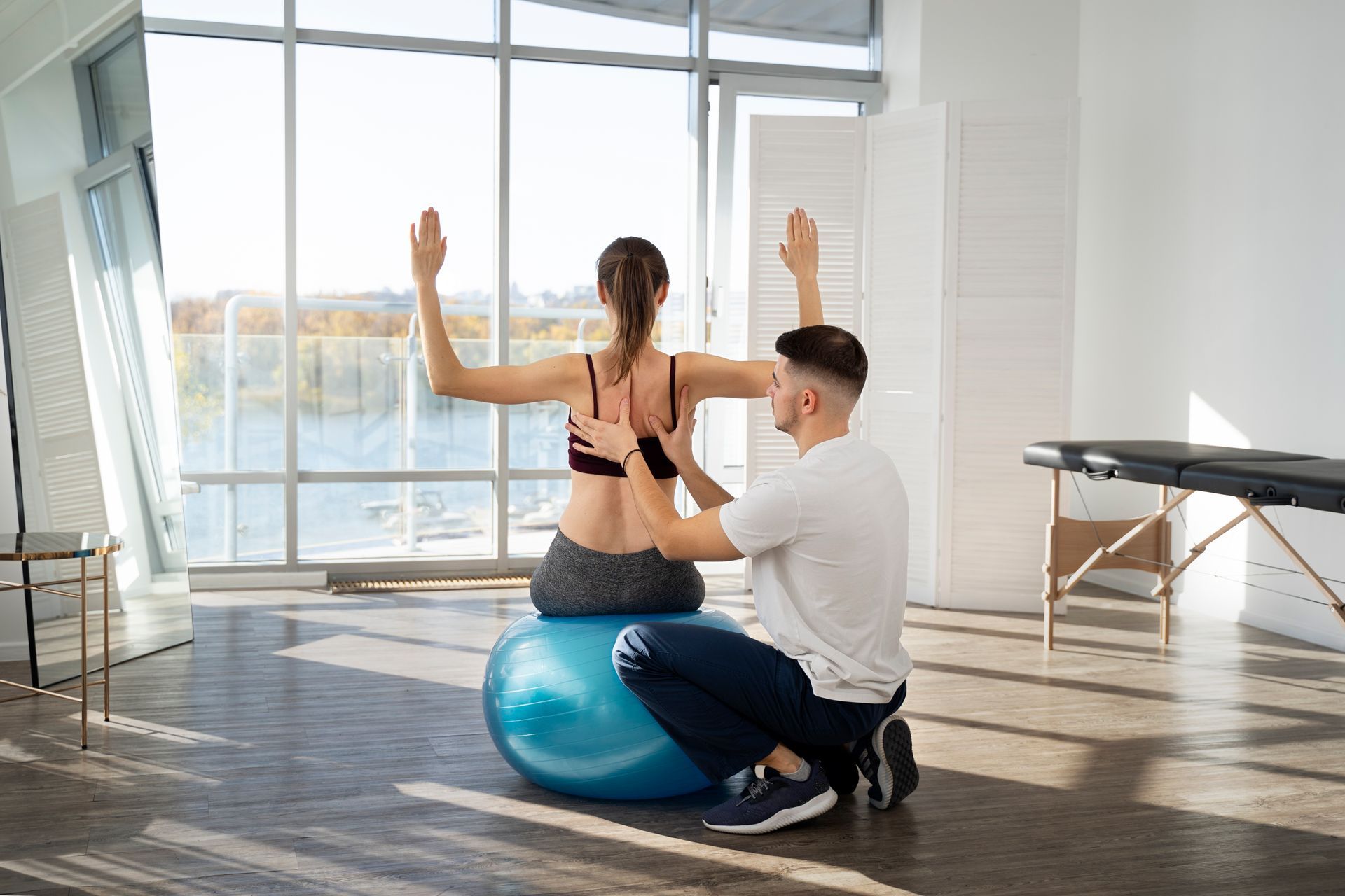 a woman sits on a blue exercise ball with her arms outstretched