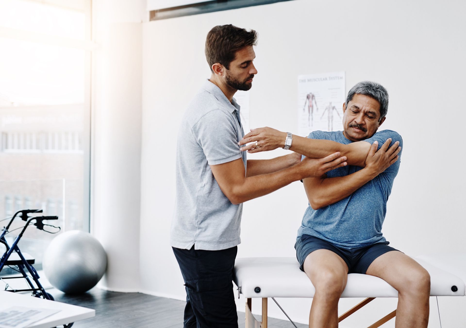 A man is sitting on a table while a man stretches his arms.