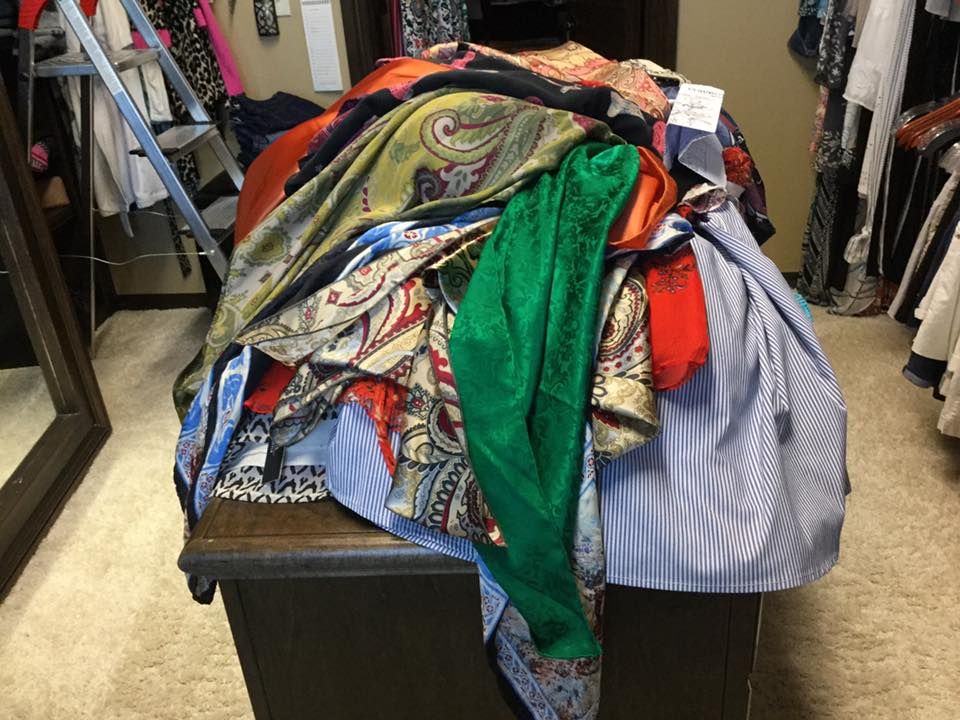 Pile of colorful scarves and clothing on a dark wooden chest in a walk-in closet.