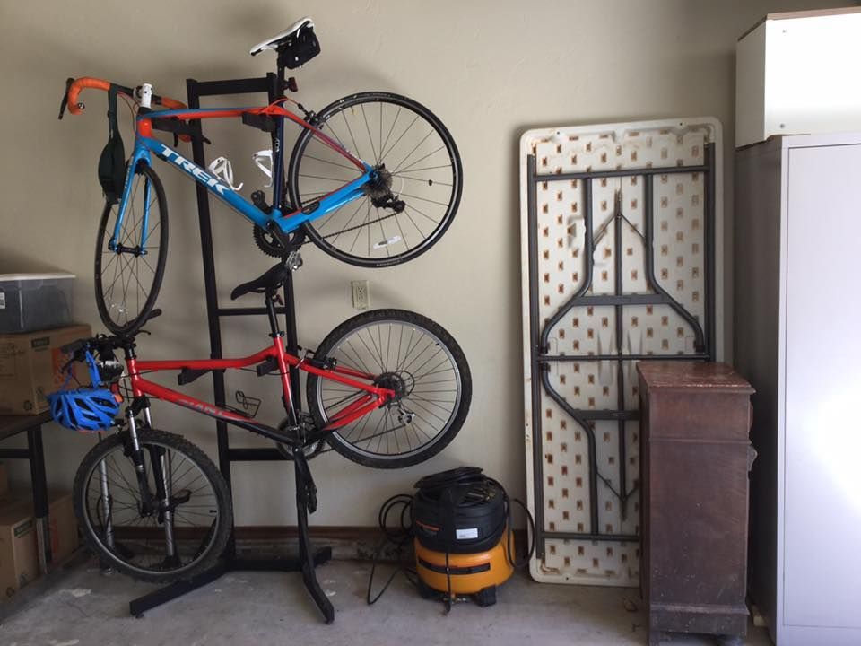 A garage with two bikes on a rack, a folding table, a cabinet, and a vacuum cleaner.