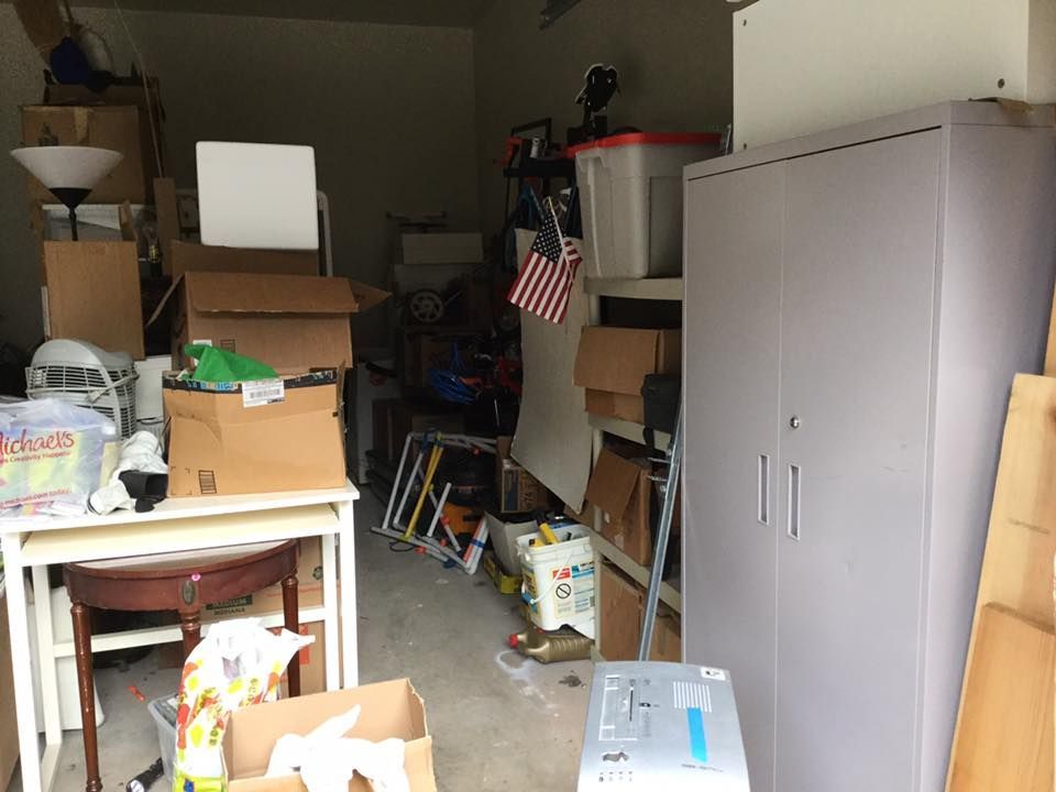 Cluttered garage with boxes, a table, cabinet, and various items.