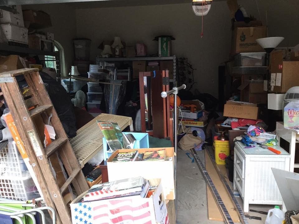 Cluttered garage interior; boxes, furniture, tools, and various items piled up and disorganized.