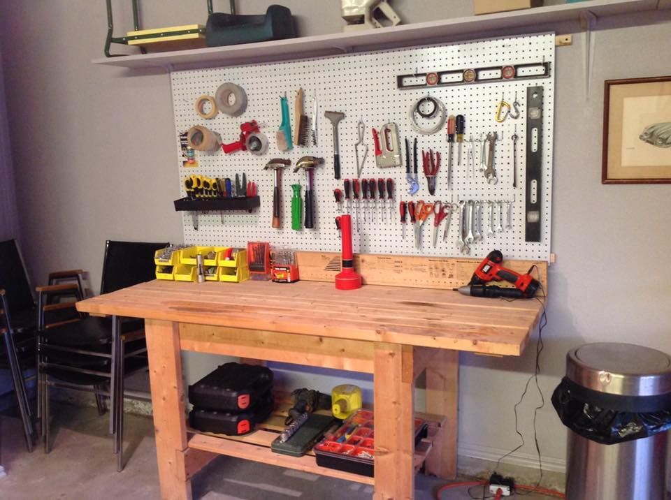 Wooden workbench with tools hanging on a pegboard, including hammers, pliers, and saws.