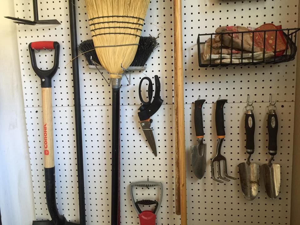 Garden tools organized on a pegboard: shovel, broom, shears, trowels, rake, and basket.