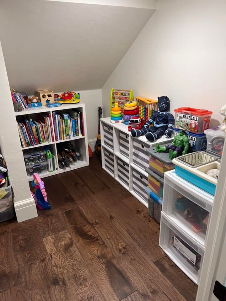 A child's playroom with bookshelves, storage bins, toys, and hardwood floors.  The room has a sloped ceiling.