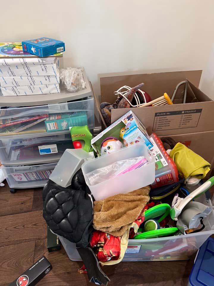 Pile of toys and boxes in a room, including a toy chest, stacked containers, and a hockey pad.