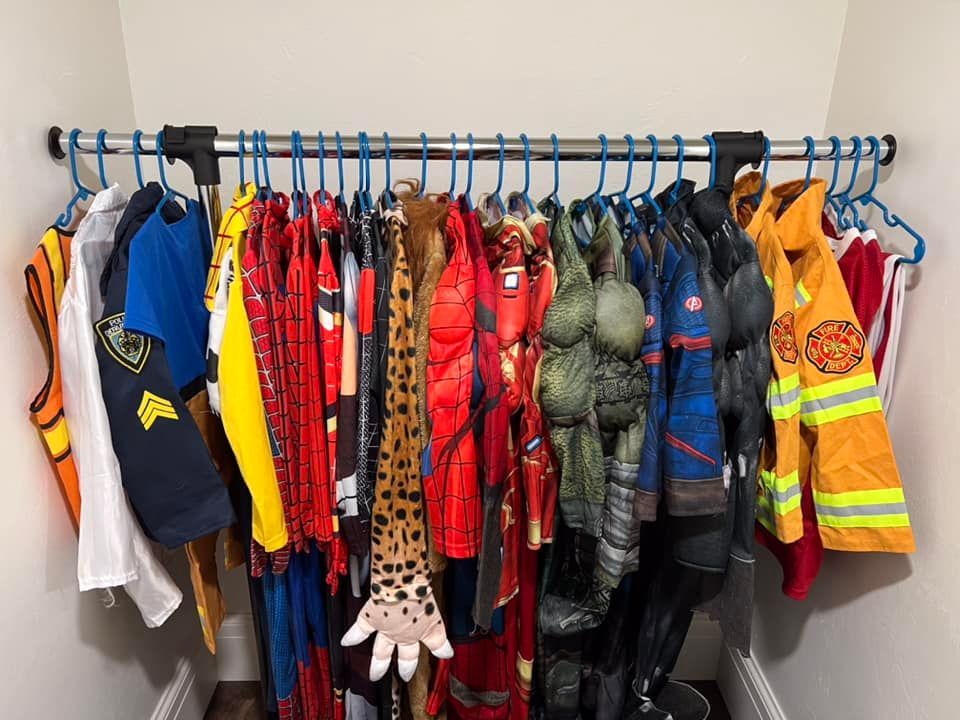 Costumes hanging on a closet rod, including police, superhero, firefighter, and animal costumes.