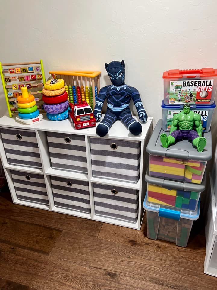 A white cube organizer with toys: abacus, stack rings, Black Panther plush, Hulk figure, and storage bins.