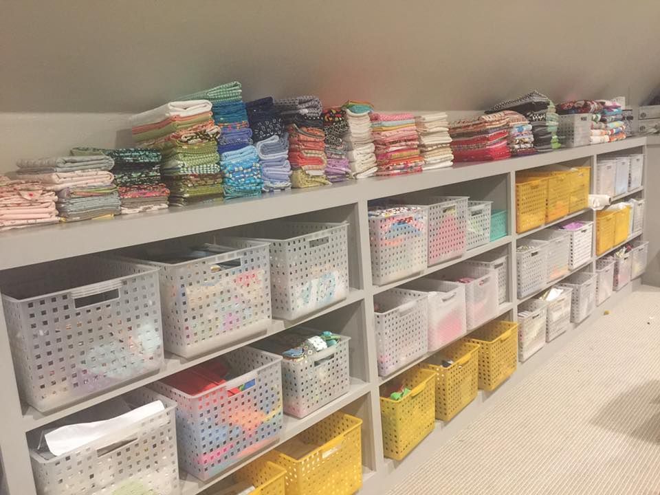 Shelves filled with organized storage bins and stacks of colorful fabric rolls in an angled attic space.