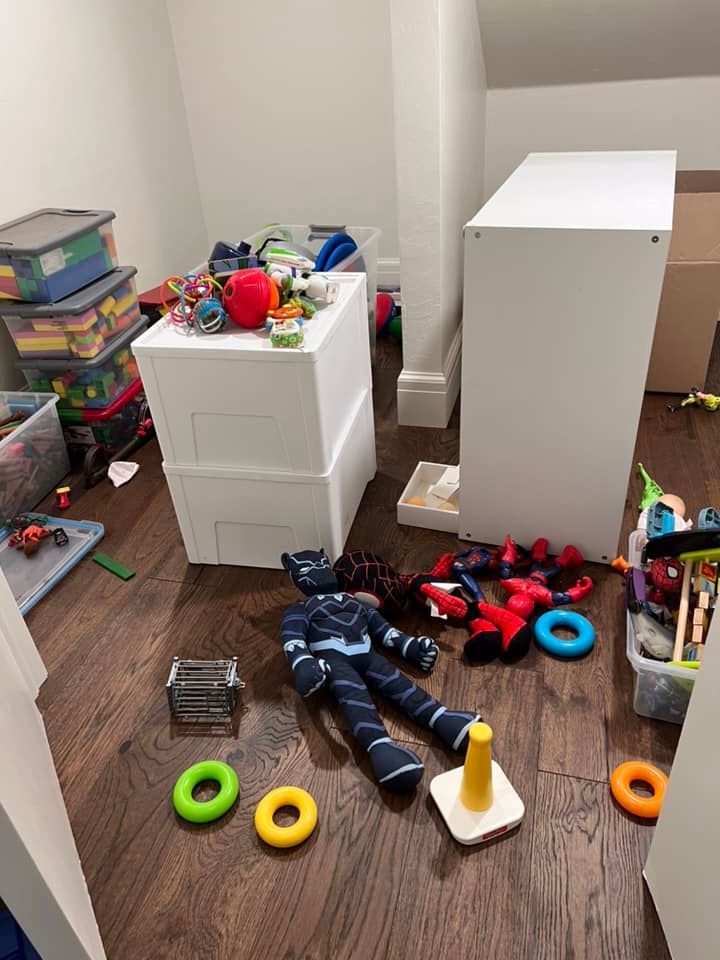 Messy playroom with toys scattered on the floor, two white storage units, and a PJ Masks toy.