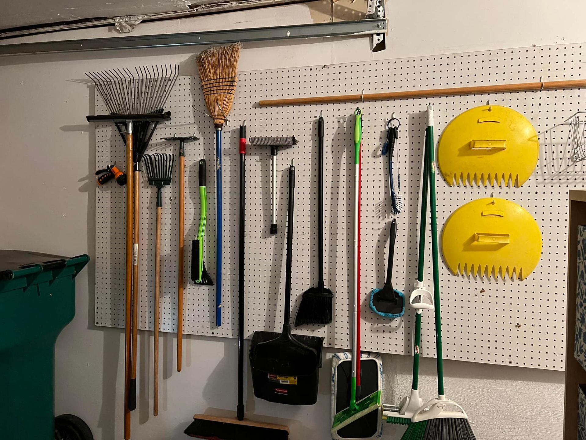 A pegboard wall in a garage holding various cleaning tools like brooms, rakes, and shovels.