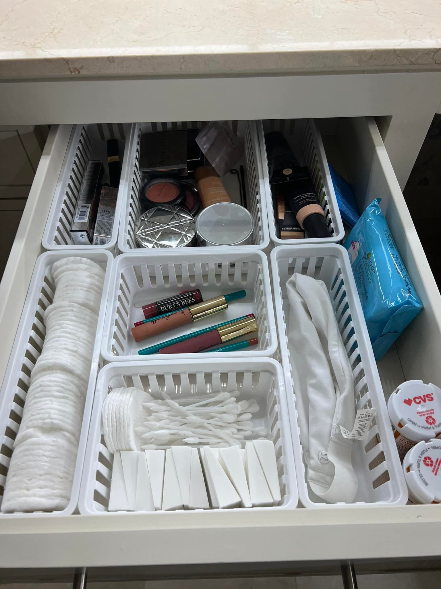 Makeup drawer with white organizers. Cotton rounds, lipstick, makeup, and q-tips are sorted.