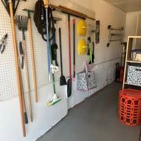 Wall-mounted tools: brooms, rakes, and other cleaning supplies. A red stool is near the wall.