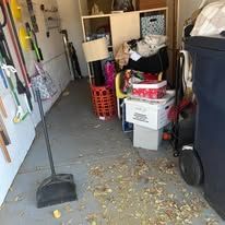 Cluttered storage area with trash, items on shelves, and a broom on the floor.
