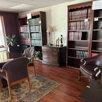 A library with wooden shelves, leather chairs, and a patterned rug on a hardwood floor.