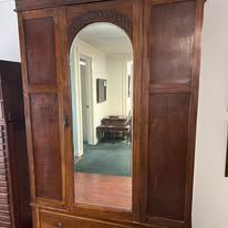 Wooden armoire with mirrored door, in a room with a green rug and tan walls.