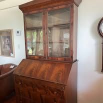 Wooden antique secretary desk with glass-doored upper cabinet, standing indoors.