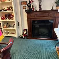 A room with a fireplace, shelf of collectibles, and a blue rug. A Santa decoration sits near the fireplace.