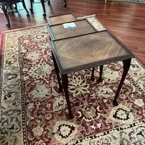 Three wooden side tables with patterned tabletops on a red floral rug.
