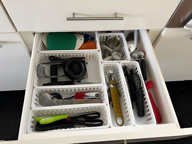 Open kitchen drawer with organized cooking utensils in white containers.